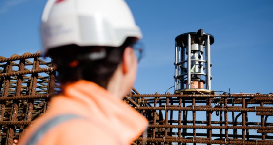 Construction worker in safety gear monitoring rebar structure with a monitoring total station on an active job site – construction safety, site monitoring, structural surveying technology